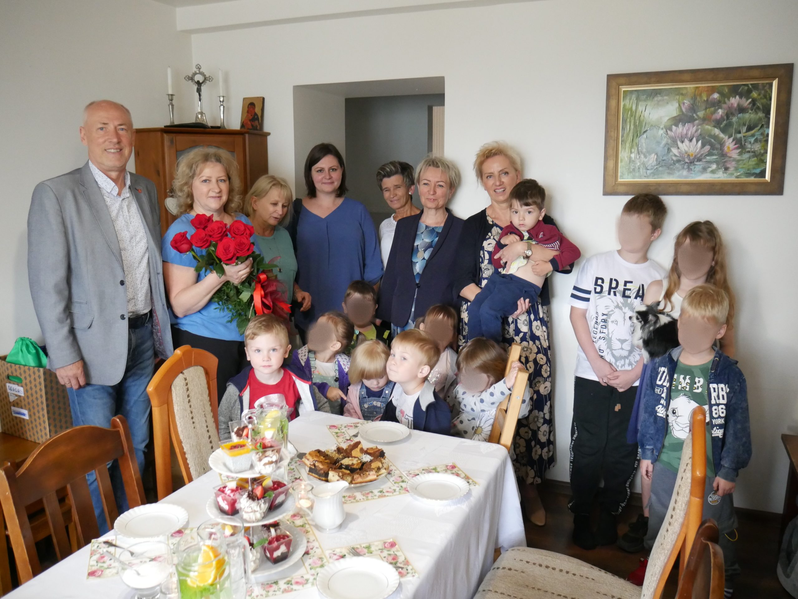Człónkowie Zarządu stoją z rodziną Kaszyca w salonie, Pani Joanna tryma kwiaty