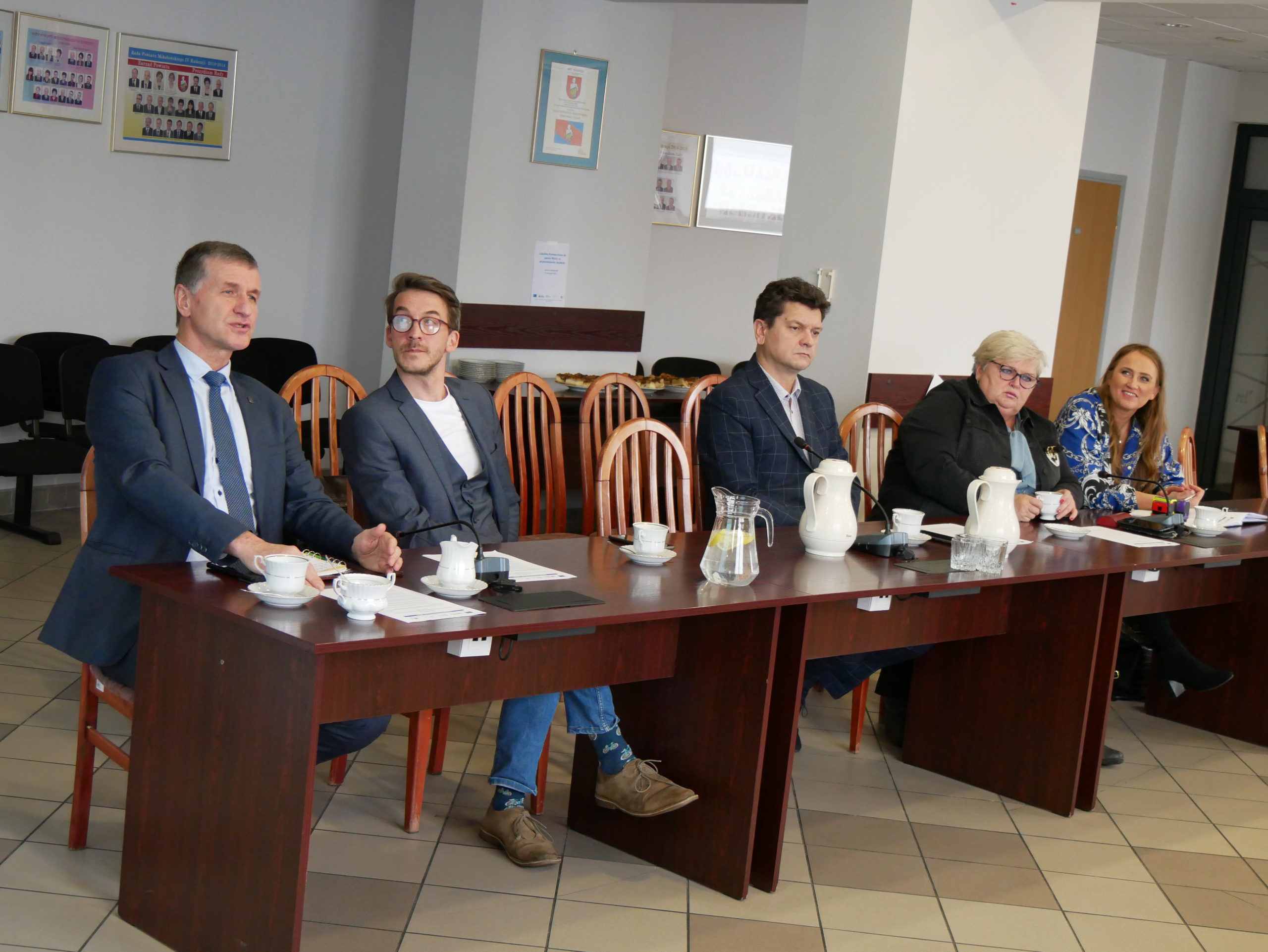 Pięciu samorządowców siedzi przy stole, a przemawia burmistrz Mikołowa